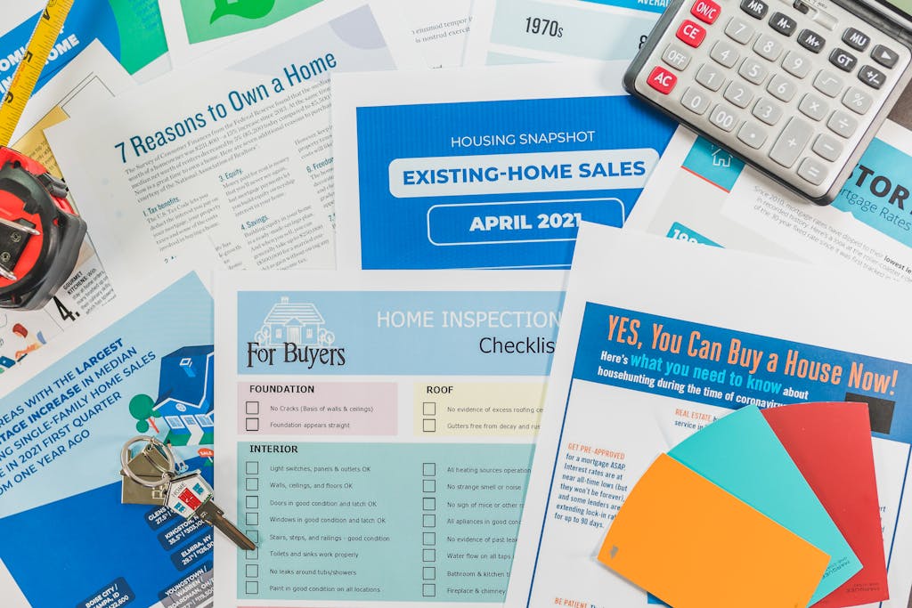 Flat lay of real estate brochures, checklists, and a calculator for home buying.