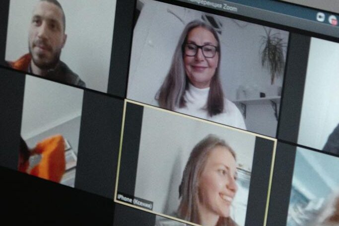 Hands at a laptop showing a group video call in a home office setting.