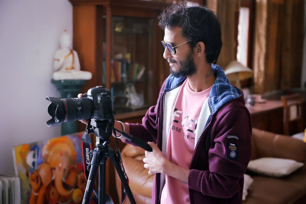Man adjusting a DSLR camera on a tripod in a cozy indoor setting.