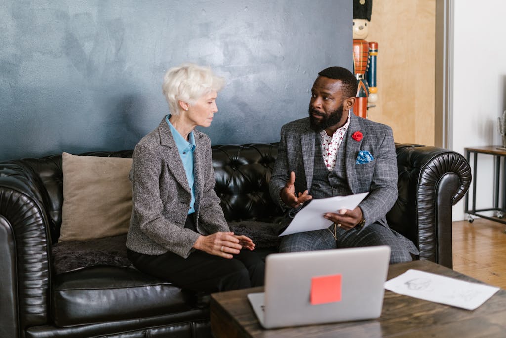 Two professionals engaged in a productive business discussion, seated on a leather couch in an office environment.
